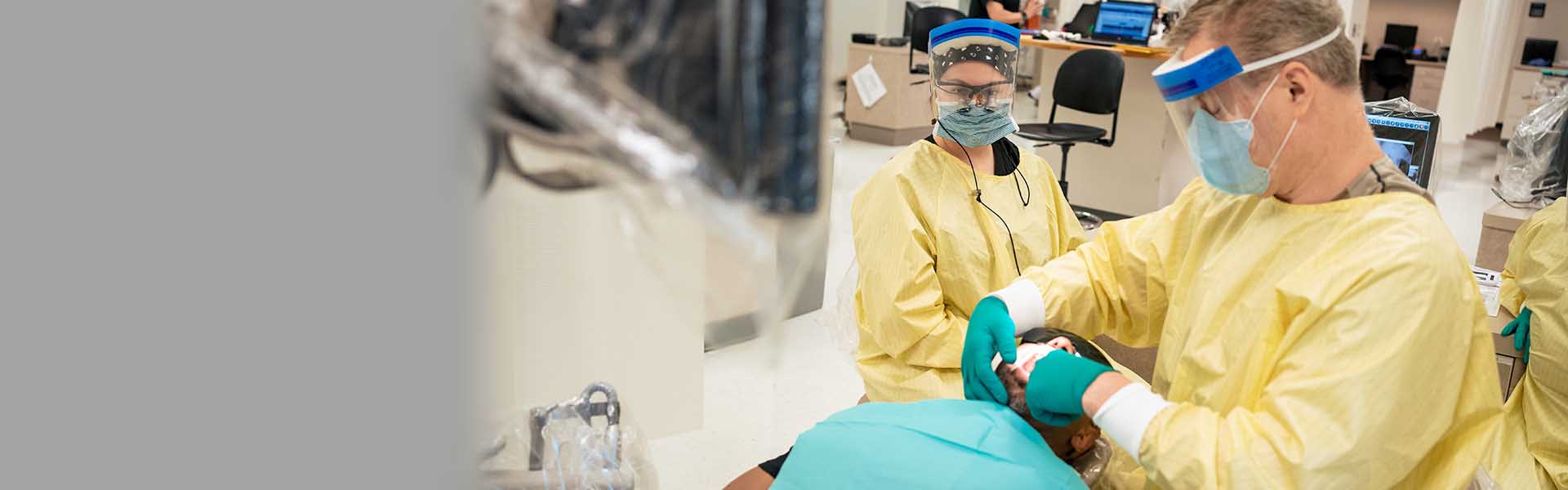 Dental Hygiene students in scrubs clean patients teeth