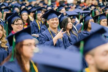 A graduate smiling and putting up the peace sign