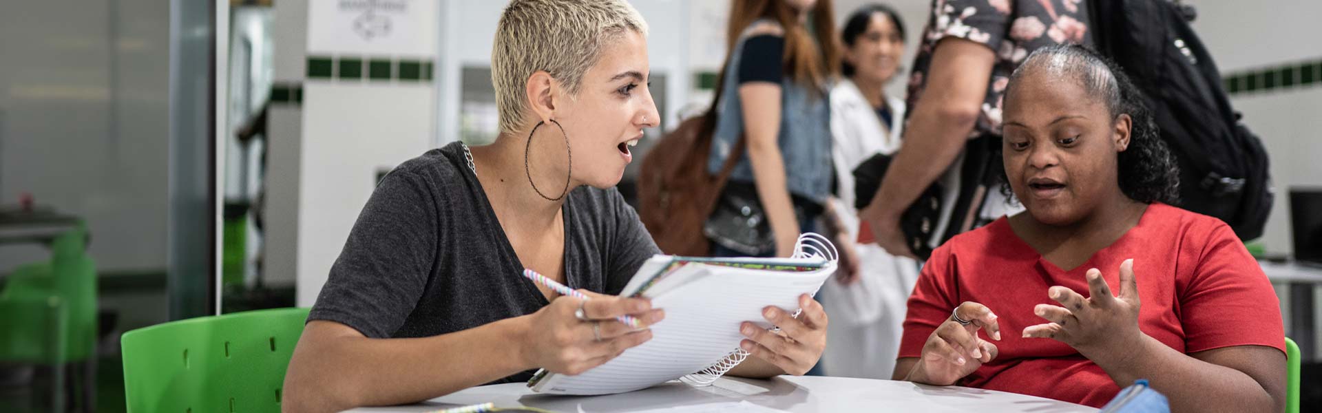 A student holding a notebook and talking with another student with Down Syndrome