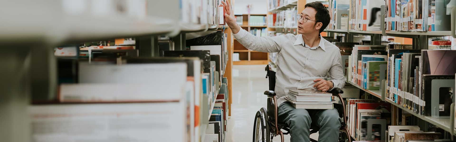A person in a wheelchair reaching for a book in a library