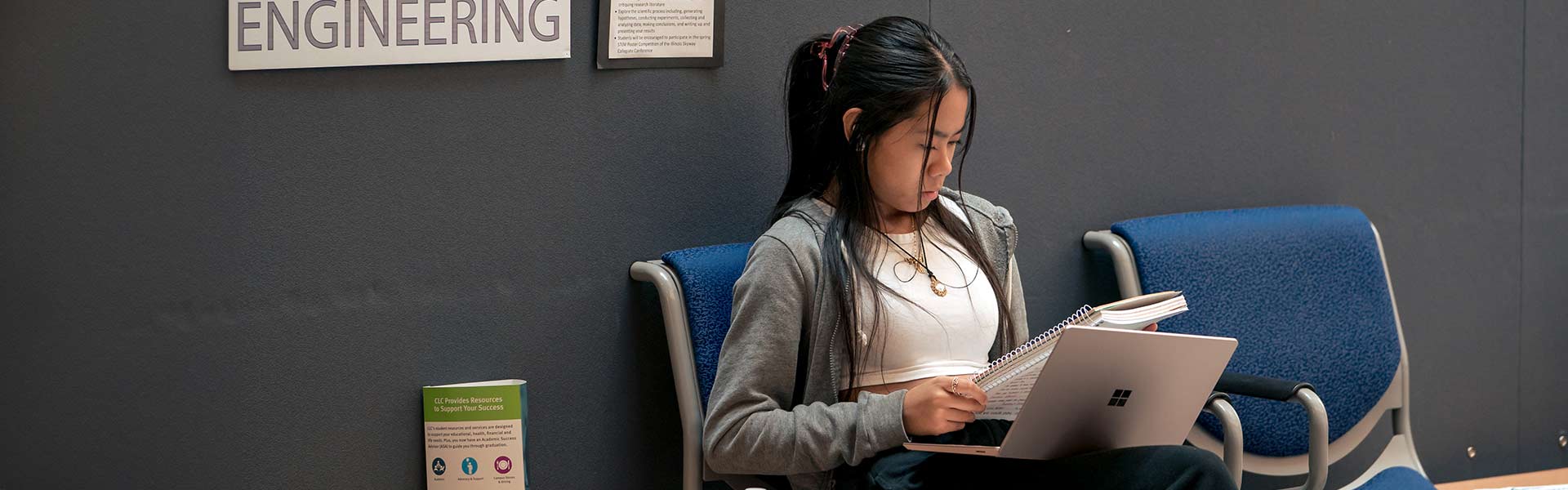 A student sitting on a hallway bench looking at their notebook