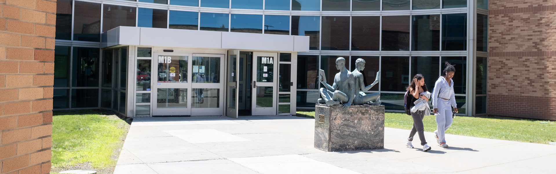 Main entrance to Grayslake Campus with two students walking past a statue of readers
