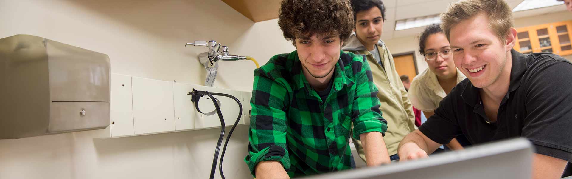 Group of four students excitedly looking at a laptop screen