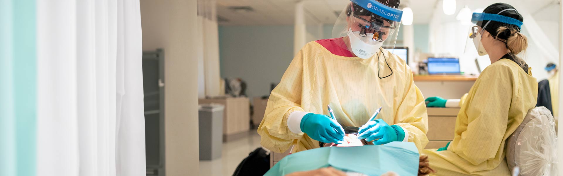 Two dental students wearing scrubs inspecting a patient's teeth
