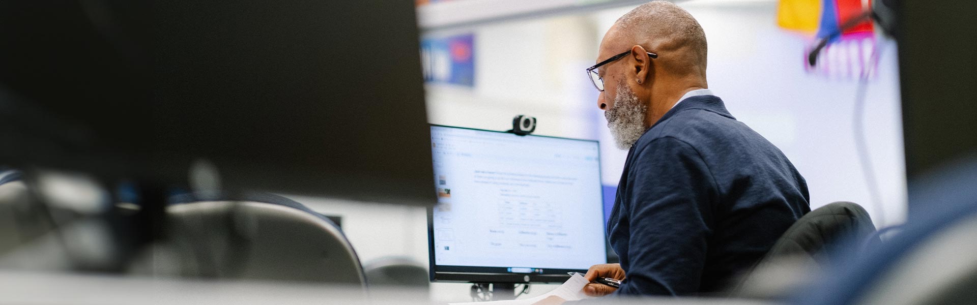 A man sits at a desk reading a computer monitor