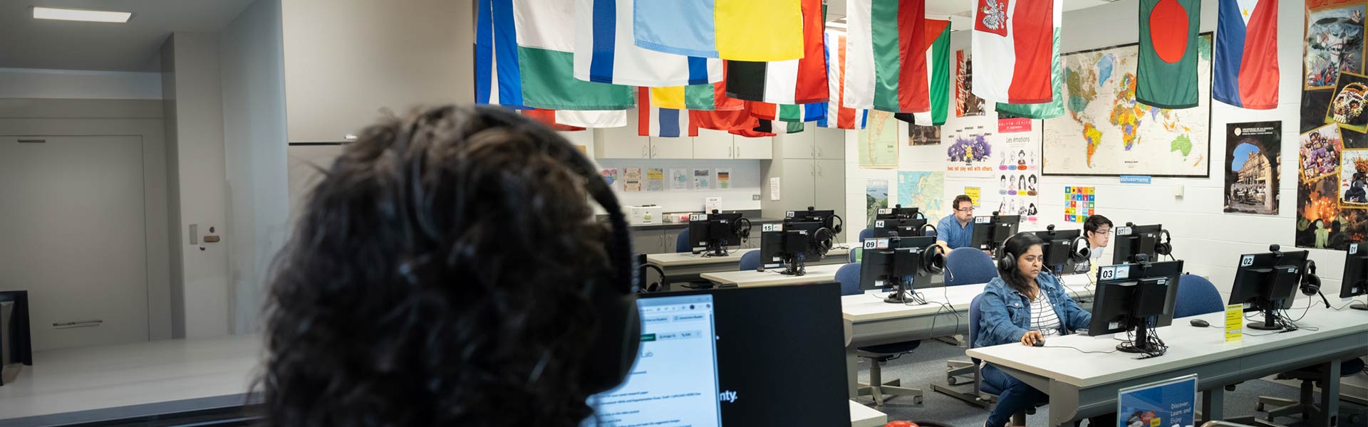 Students working in the language lab, sitting at computers with colorful flags overhead.