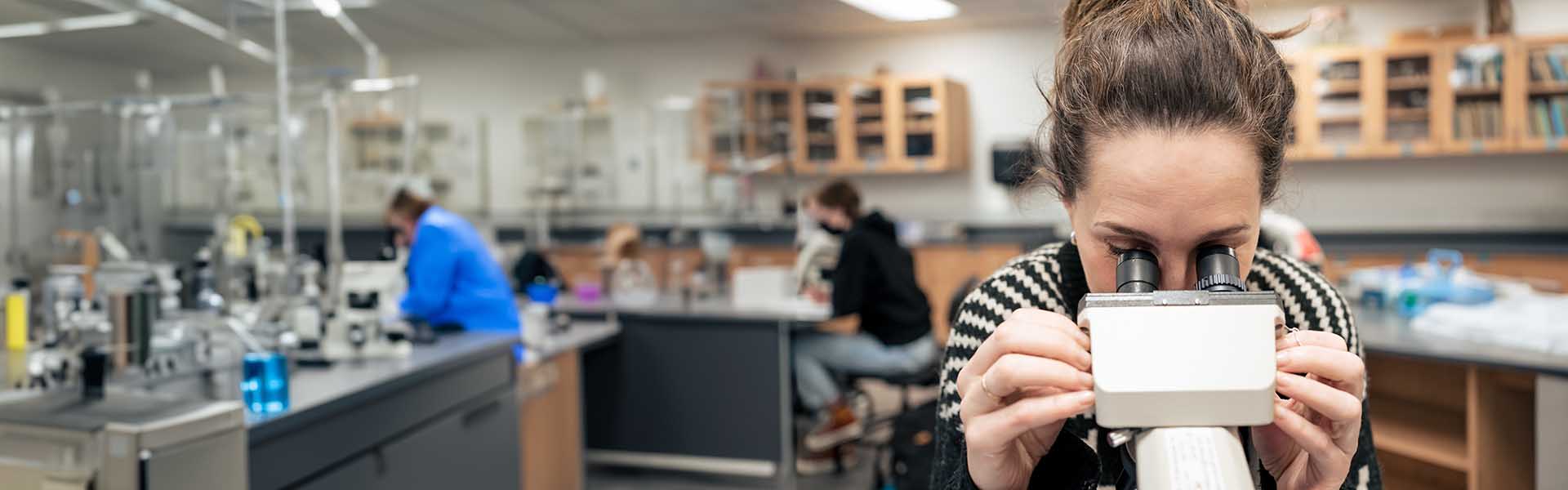 Student in a science lab and looking into a microscope.