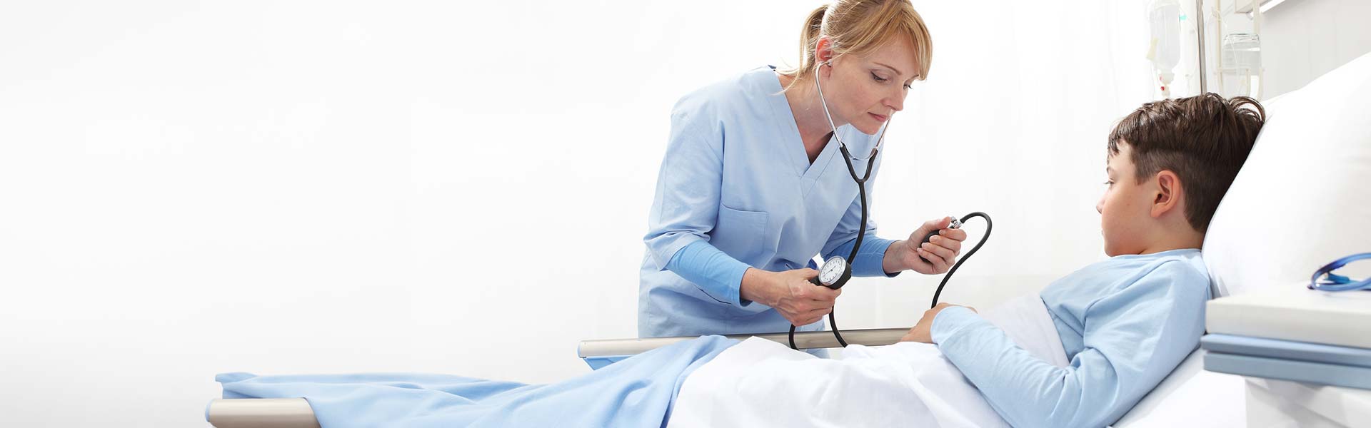 Medical assisting student taking a young boy's blood pressure reading in a hospital room.