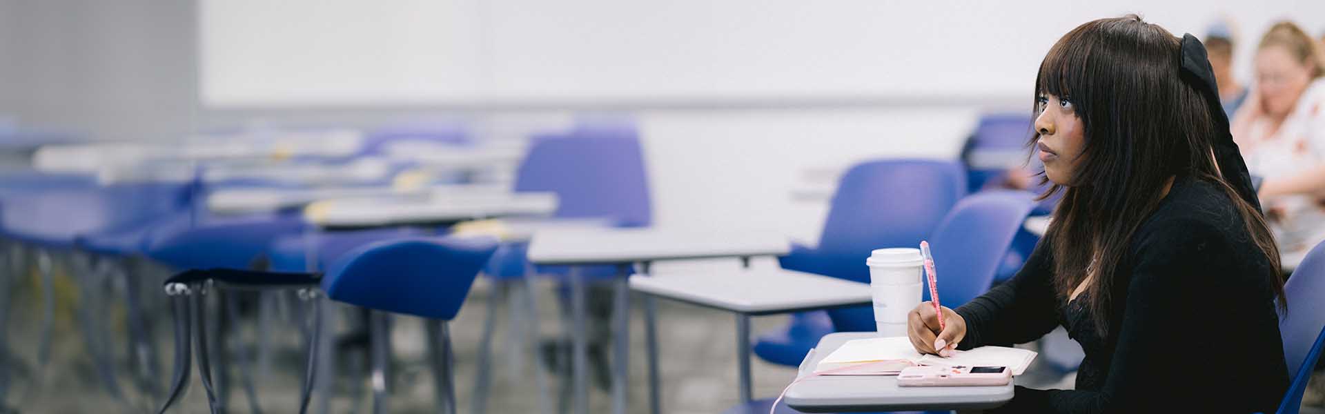 Female African-American student listening to lecture in class and taking notes on her notebook