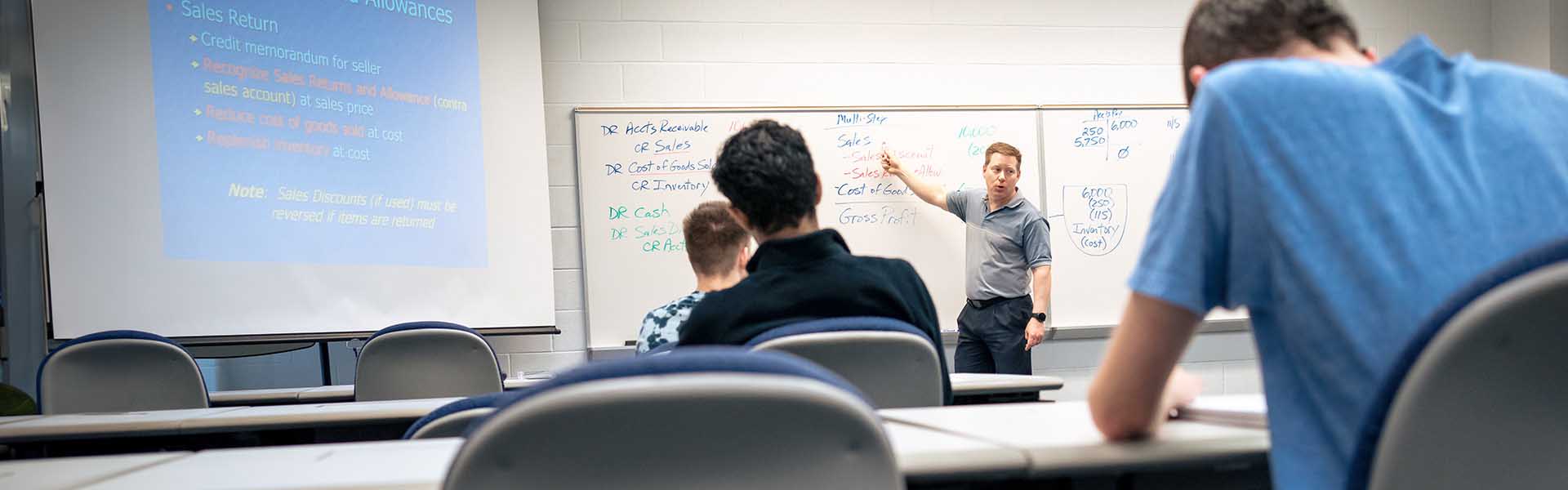 CLC instructor pointing to his notes on the whiteboard in front of students in class