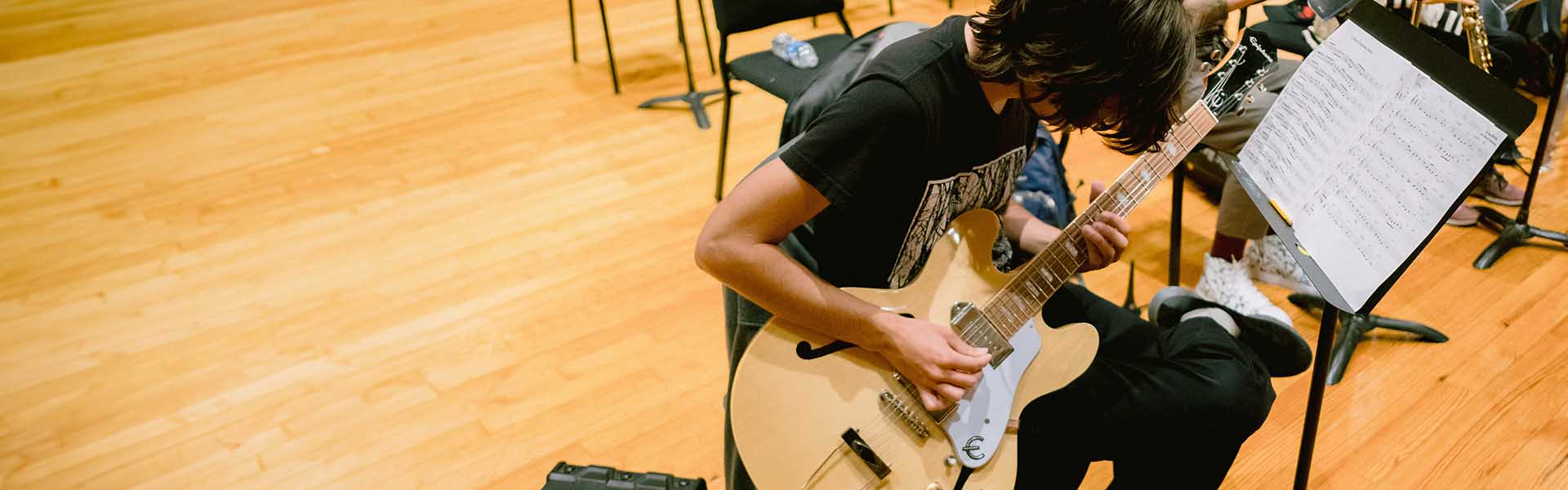 Male Music student practicing on his guitar in class