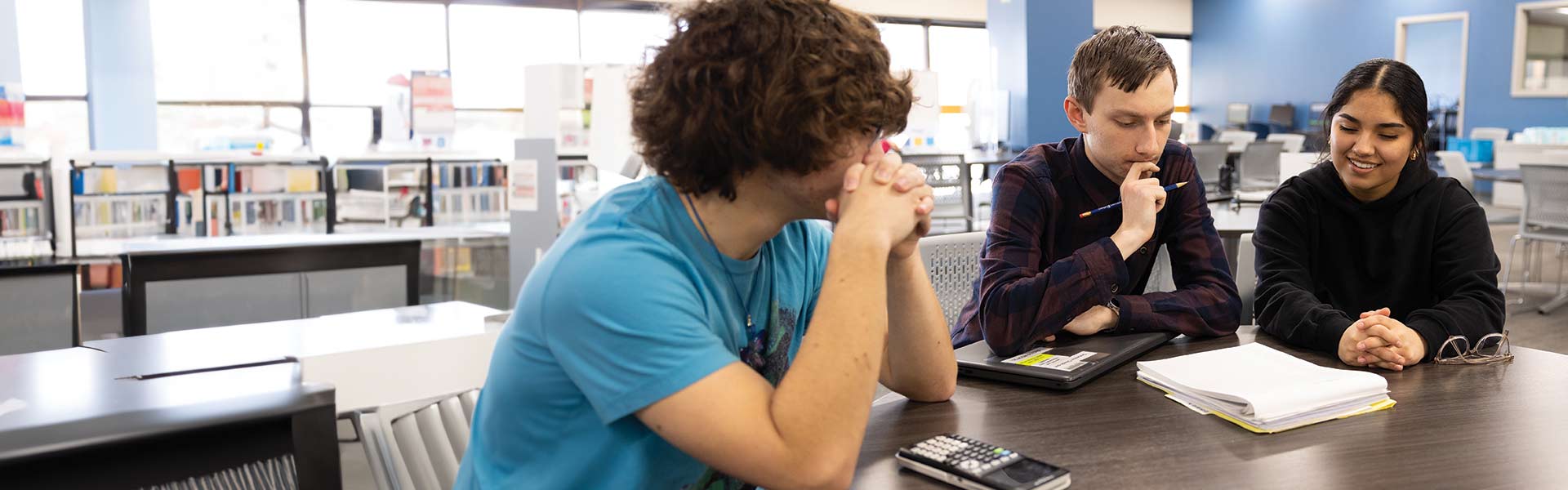 Two students and a tutor working on homework in a library