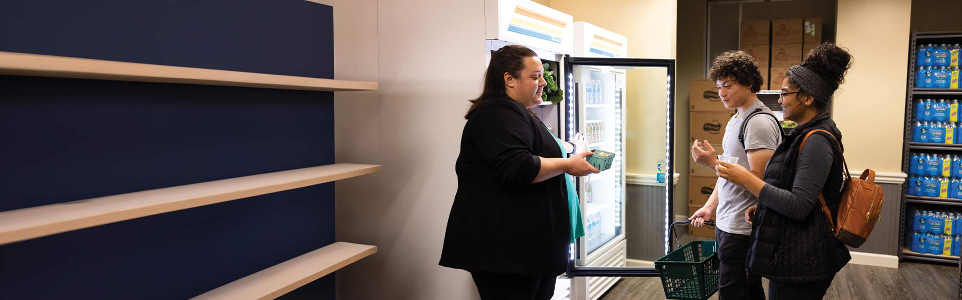 Two students and a worker are talking in front of a fridge holding food in the Share Market