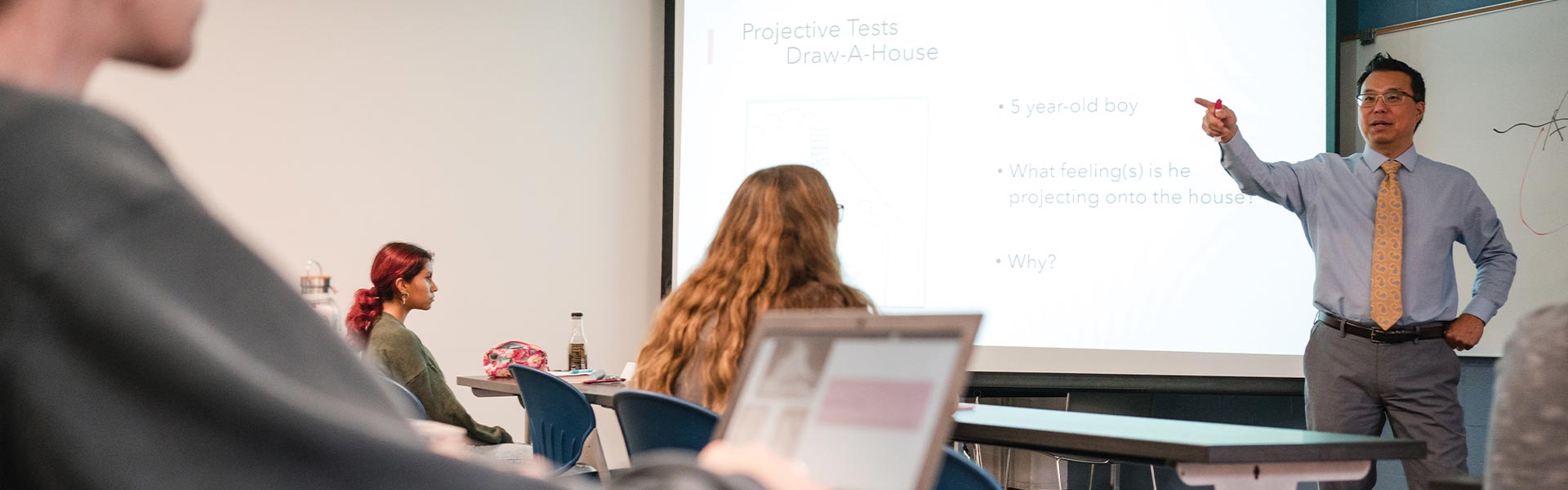 A teacher talking to his class in front of a screen