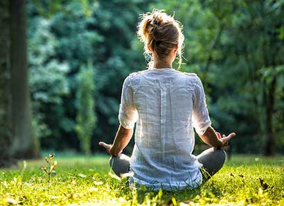 Women meditates in a sunny patch of grass