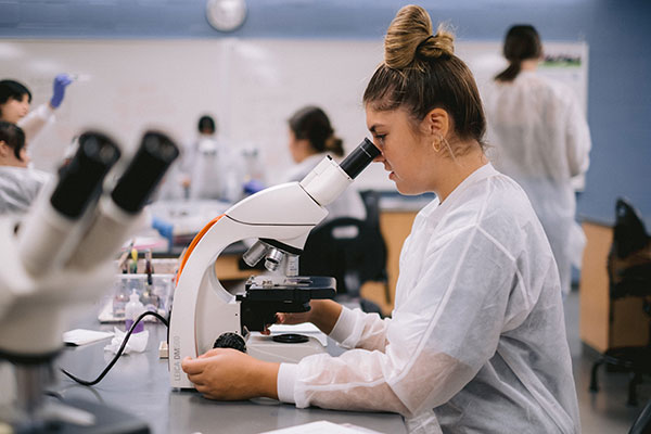 Student in lab coat looking through a microscope