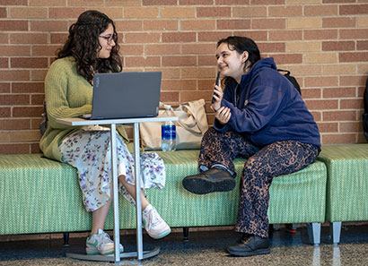 Two female students sitting on a bench, sharing stories.