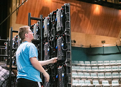 Student working technology panels behind the stage with view of theatre seating