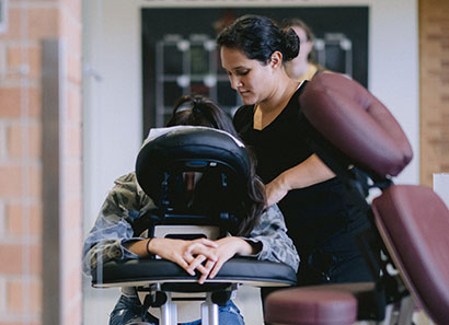 Female Latinx student performing chair massage to fellow student