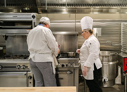 Chef instructor and student at stove, kitchen classroom at Grayslake Campus