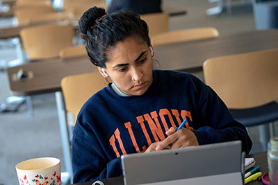 Student wearing University of Illinois sweatshirt studying in library