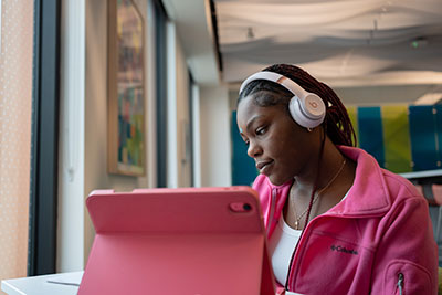 Female student in pink sweater looking at pink laptop