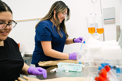 Two students in scrubs practicing phlebotomy skills