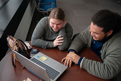 Two students smiling while looking at laptop