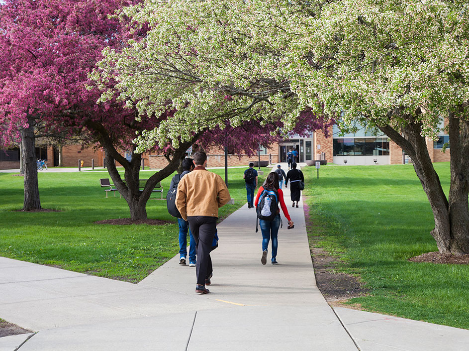 Students entering Grayslake Campus building with blooming spring trees lining sidewalk