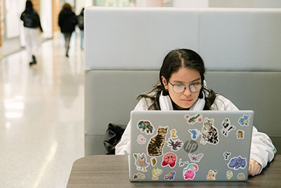 A student intently looking at her laptop, which is covered in stickers