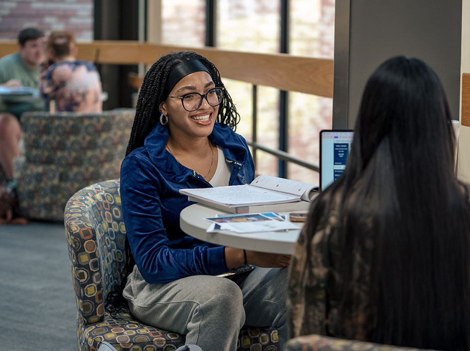 Two students studying at table, smiling.