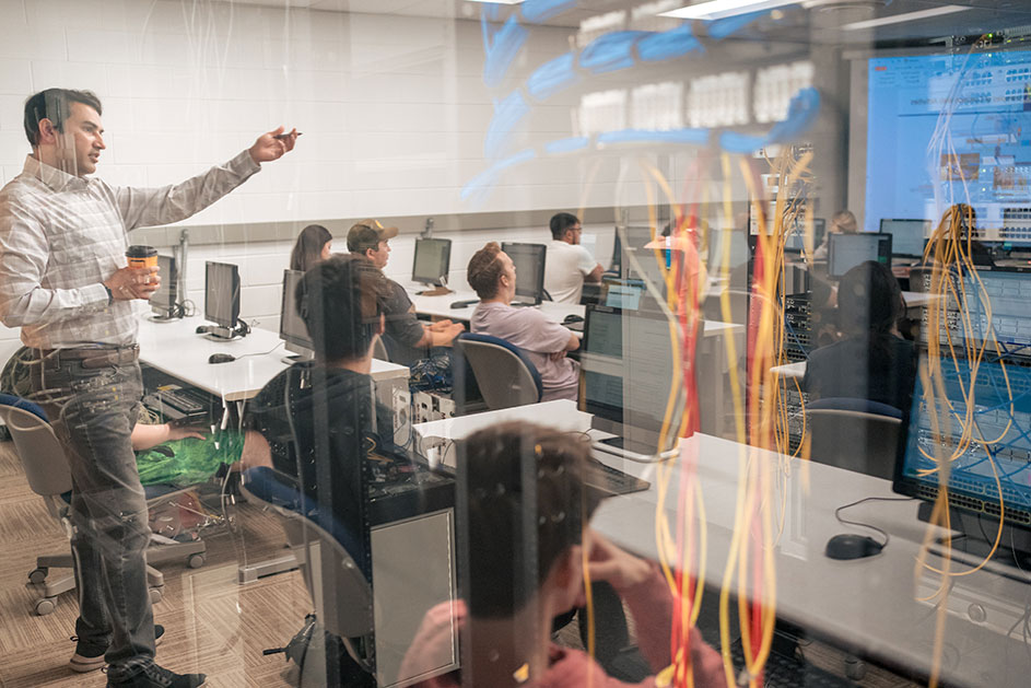 View of students in class with IT servers reflected in glass