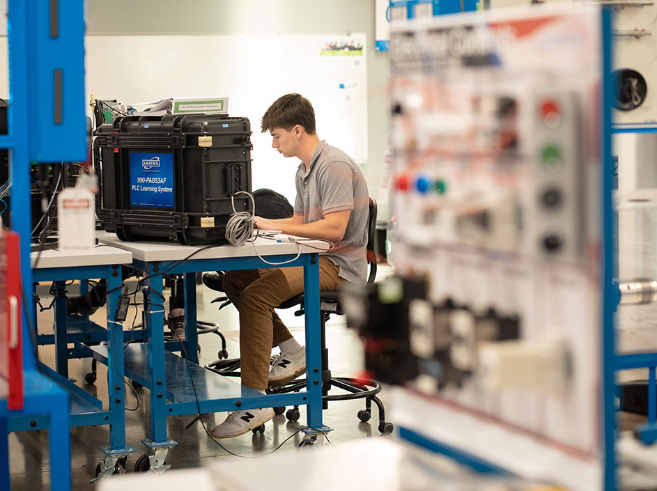 Student seated at workbench, programming equipment