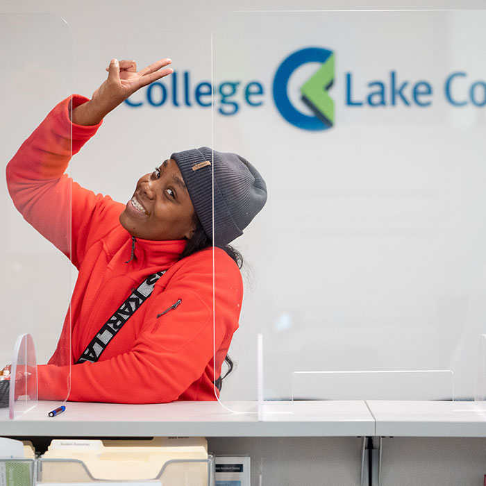 A woman giving the peace sign while standing at the Southlake Campus Welcome and One Stop Center counter